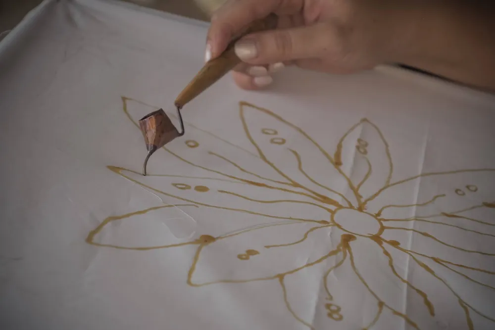 A canting drawing a flower motif in hot wax on white cotton