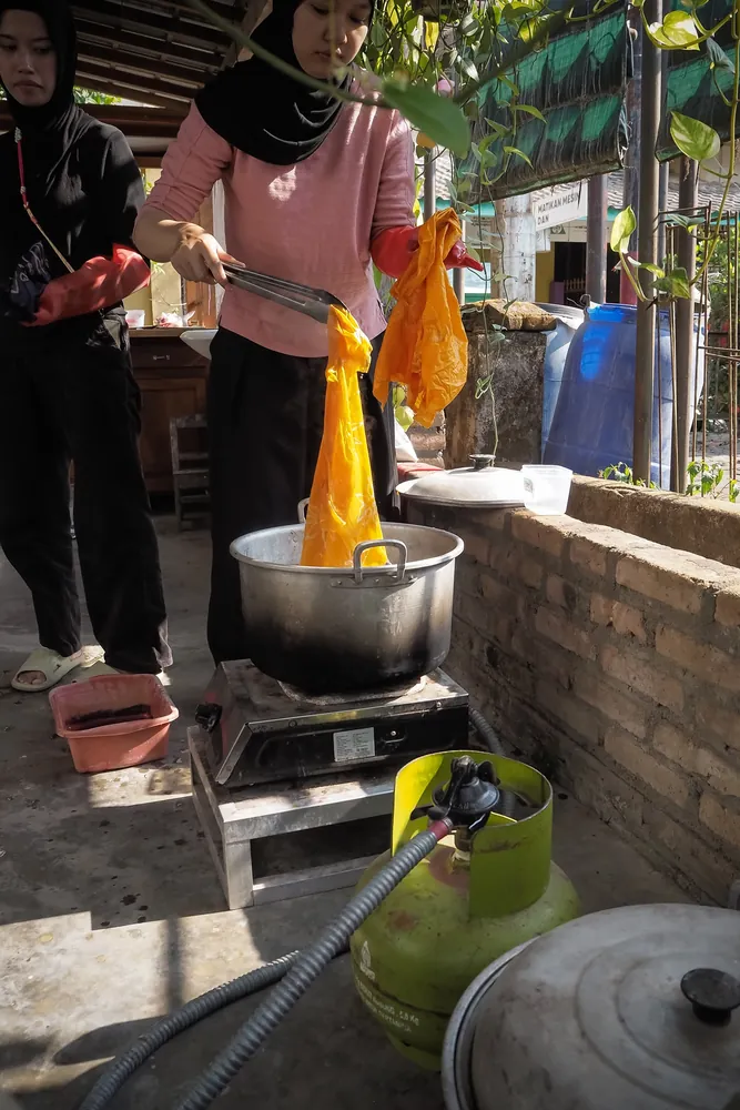 Lifting a bright yellow cloth out of the boiling pot as the wax comes away