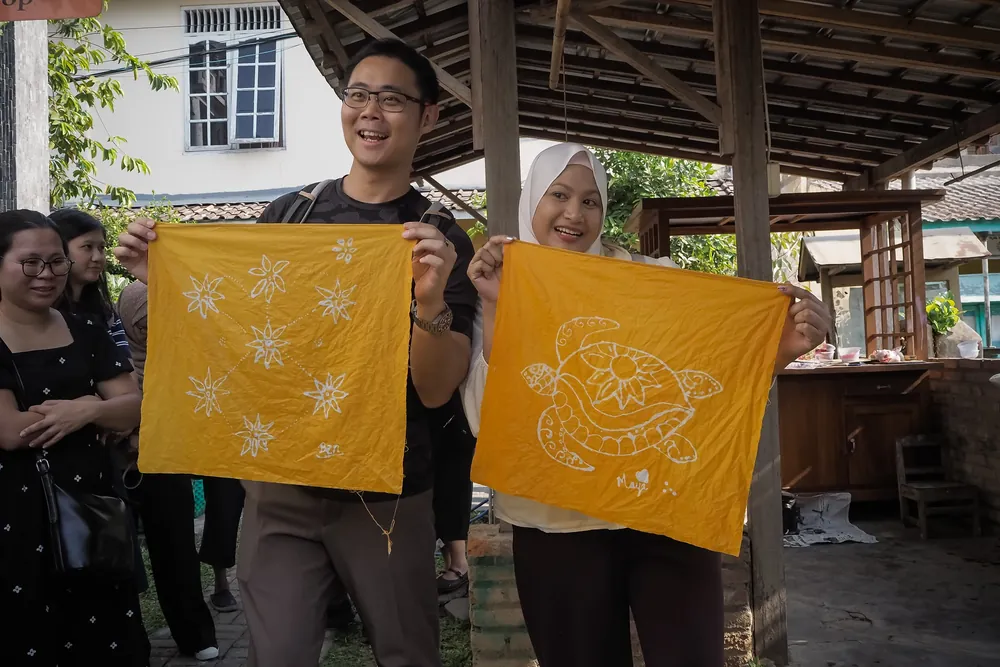 Two guests holding up the batik cloths they drew and dyed at a batik workshop in Jogja